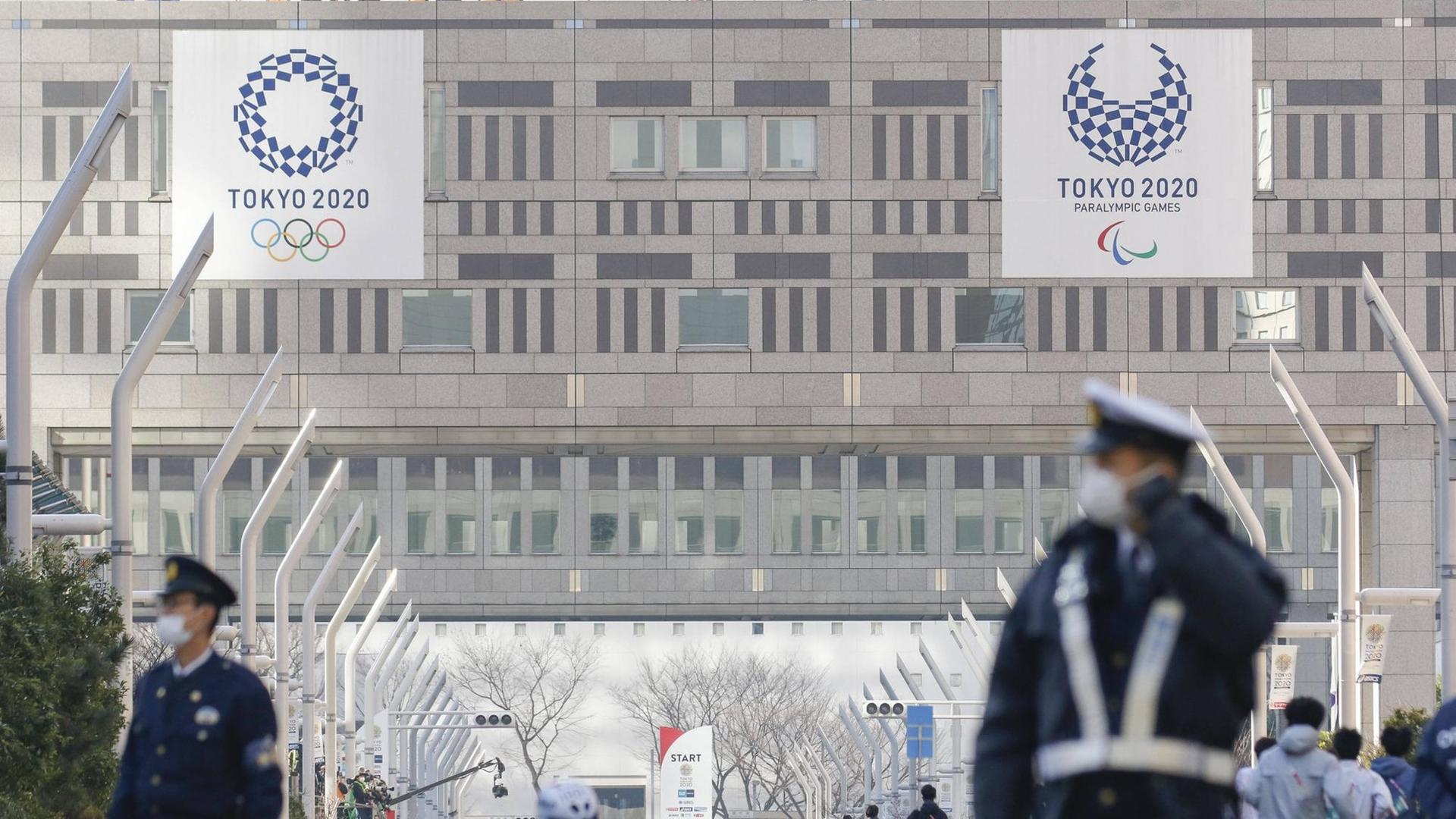 Sicherheitskräfte mit Mundschutz in Tokio vor den Bannern der Olympischen und der Paralympischen Spiele 2020. Sicherheitskräfte mit Mundschutz in Tokio vor den Bannern der Olympischen und der Paralympischen Spiele 2020.