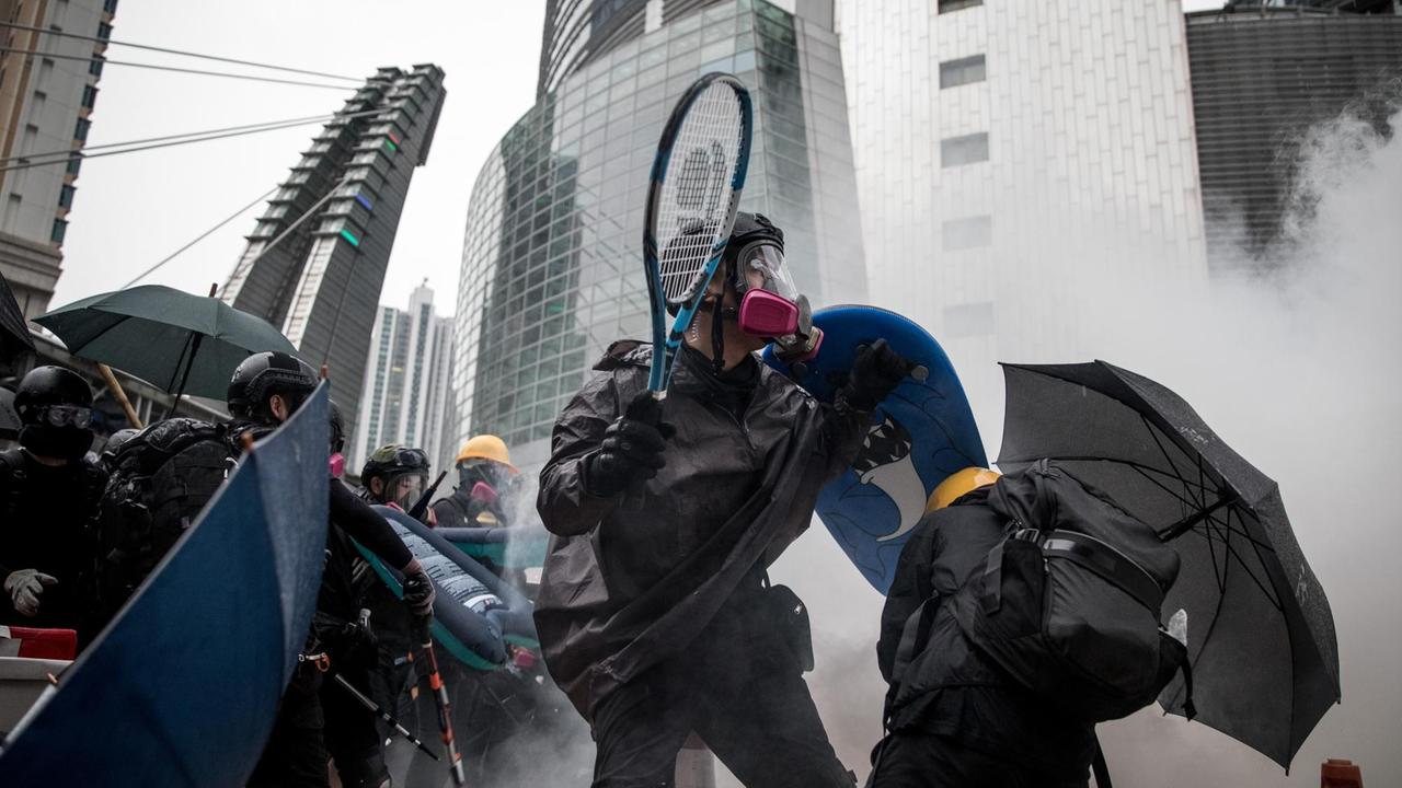 Ein Demonstrat stellt sich mit Helm, Schutzmaske und einem Tennischschläger in der Hand der Polizeit und dem aufkommden Rauch entgegen. Ein Demonstrat stellt sich mit Helm, Schutzmaske und einem Tennischschläger in der Hand der Polizeit und dem aufkommden Rauch entgegen.