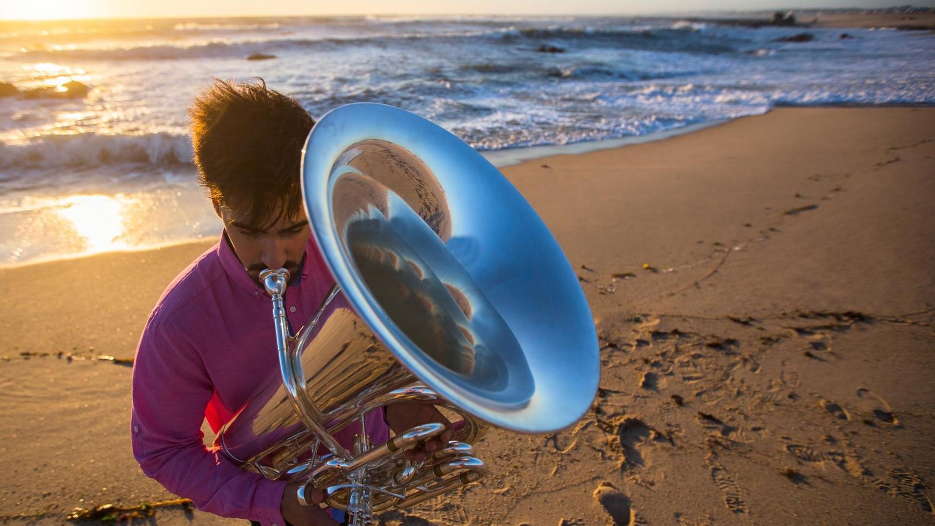 Ein Tubist spielt am Strand, in dem sich viele Fußabdrücke abzeichnen. Ein Tubist spielt am Strand, in dem sich viele Fußabdrücke abzeichnen.