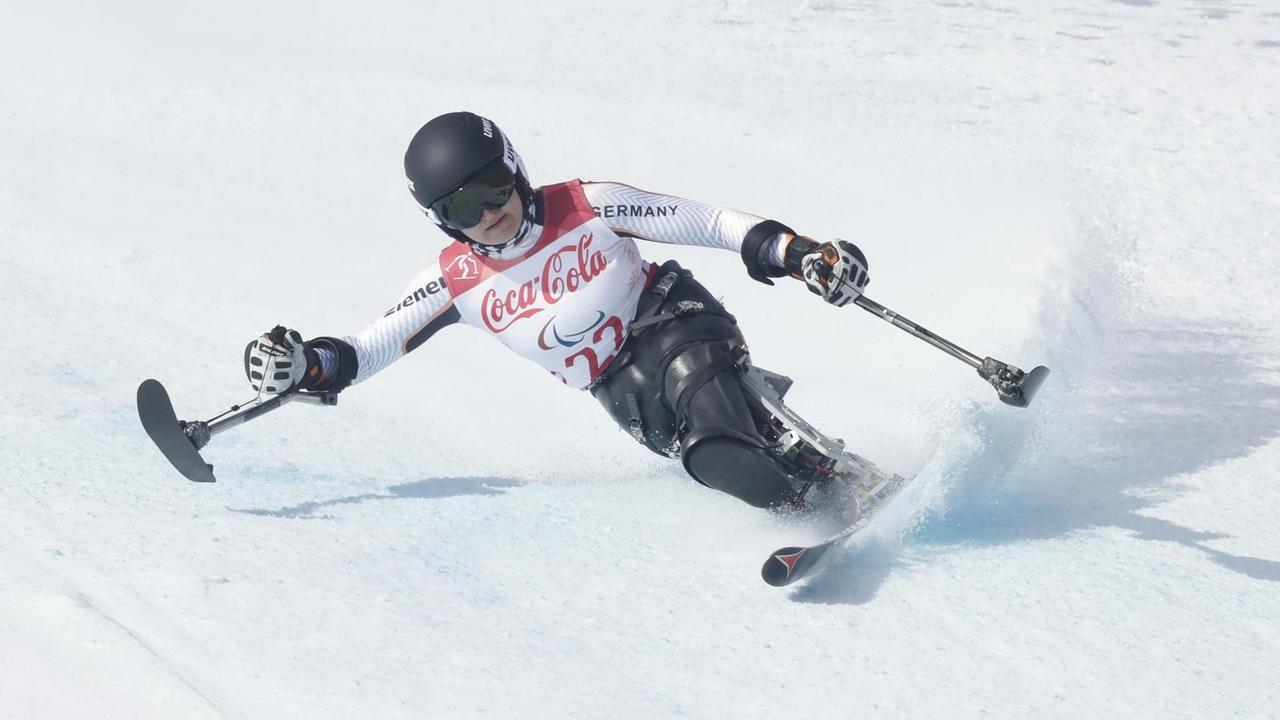 Forster liegt auf dem weißen Schnee in der Kurve. In den Händen hält sie kurze Stöcke mit Laufflächen. Forster liegt auf dem weißen Schnee in der Kurve. In den Händen hält sie kurze Stöcke mit Laufflächen.