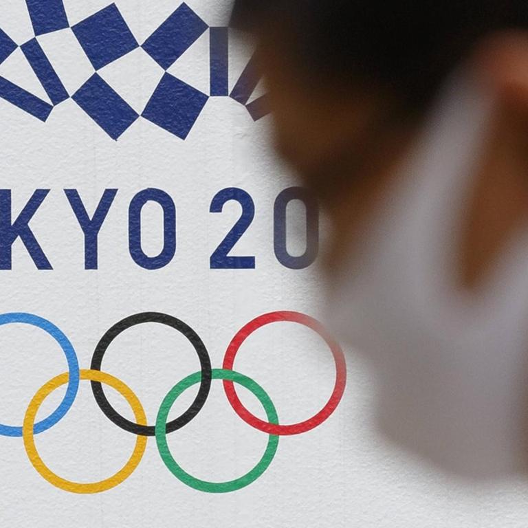 Ein Man mit Gesichtsmaske geht an einem Logo für die Olympischen Spiele in Tokio 2020 vorbei.