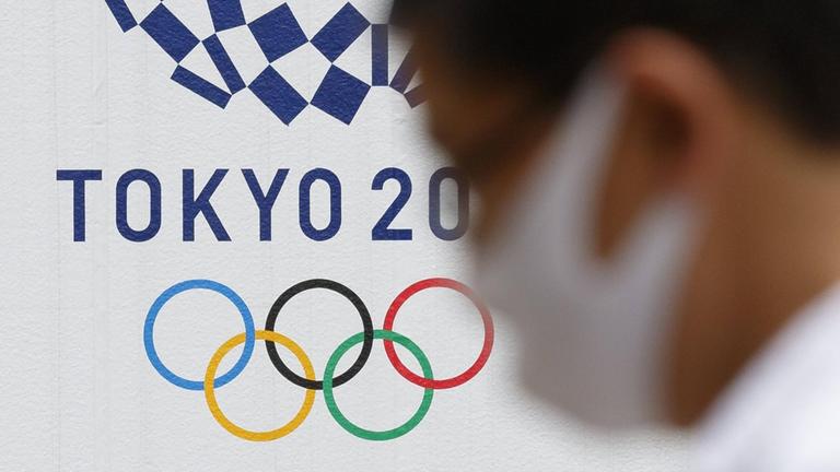 Ein Man mit Gesichtsmaske geht an einem Logo für die Olympischen Spiele in Tokio 2020 vorbei.