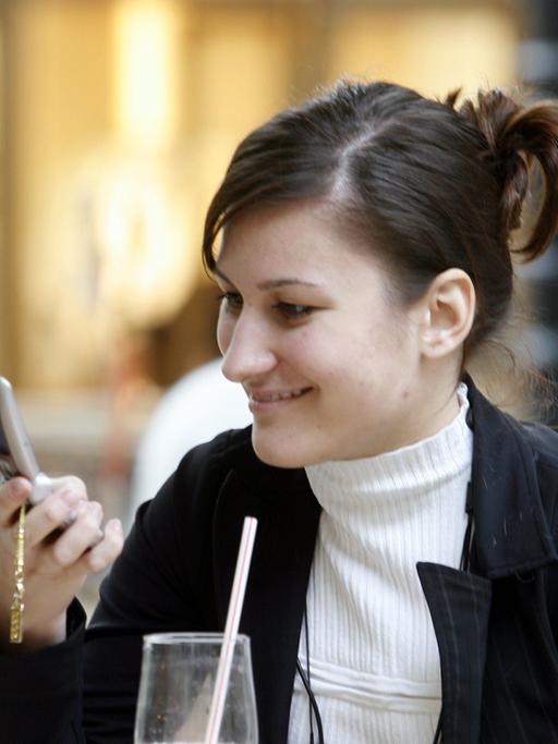 Eine junge Frau schaut auf ihr Mobiltelefon, während sie in einem Cafe sitzt. 