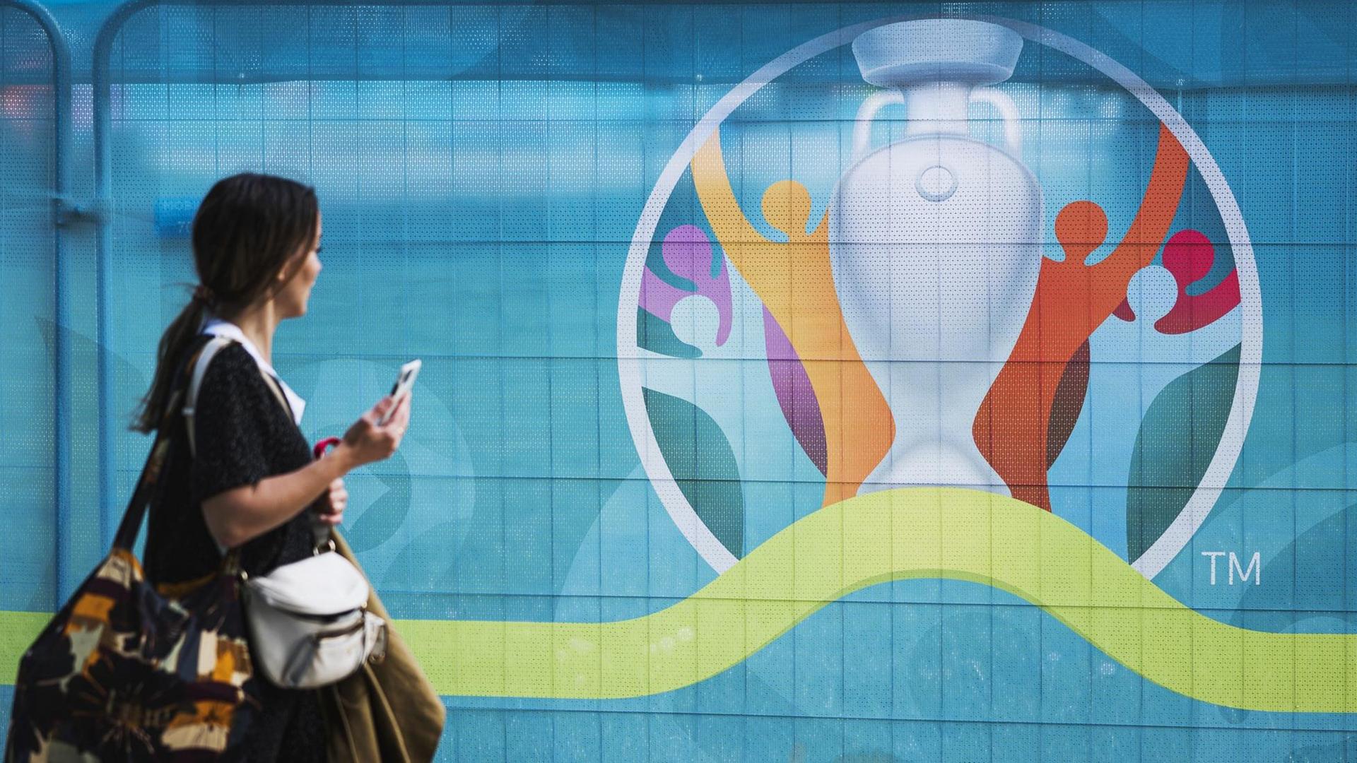 Eine Passantin geht in Kopenhagen am Logo der Fußball-Europameisterschaft UEFA EURO 2020/2021 vorbei, das an einem Bauzaun befestigt ist. Kopenhagen ist einer der Austragungsstädte des Turniers. Eine Passantin geht in Kopenhagen am Logo der Fußball-Europameisterschaft UEFA EURO 2020/2021 vorbei, das an einem Bauzaun befestigt ist. Kopenhagen ist einer der Austragungsstädte des Turniers.