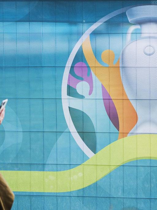 Eine Passantin geht in Kopenhagen am Logo der Fußball-Europameisterschaft UEFA EURO 2020/2021 vorbei, das an einem Bauzaun befestigt ist. Kopenhagen ist einer der Austragungsstädte des Turniers.