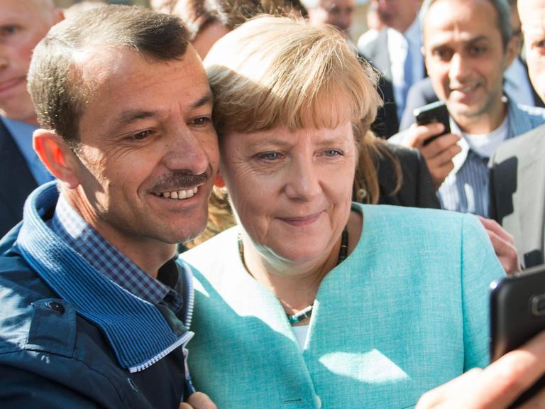 Bundeskanzlerin Angela Merkel (CDU) lässt sich am 10.09.2015 nach dem Besuch einer Erstaufnahmeeinrichtung für Asylbewerber der Arbeiterwohlfahrt (AWO) und der Außenstelle des Bundesamtes für Migration und Flüchtlinge in Berlin-Spandau für ein Selfie zusammen mit einem Flüchtling fotografieren.