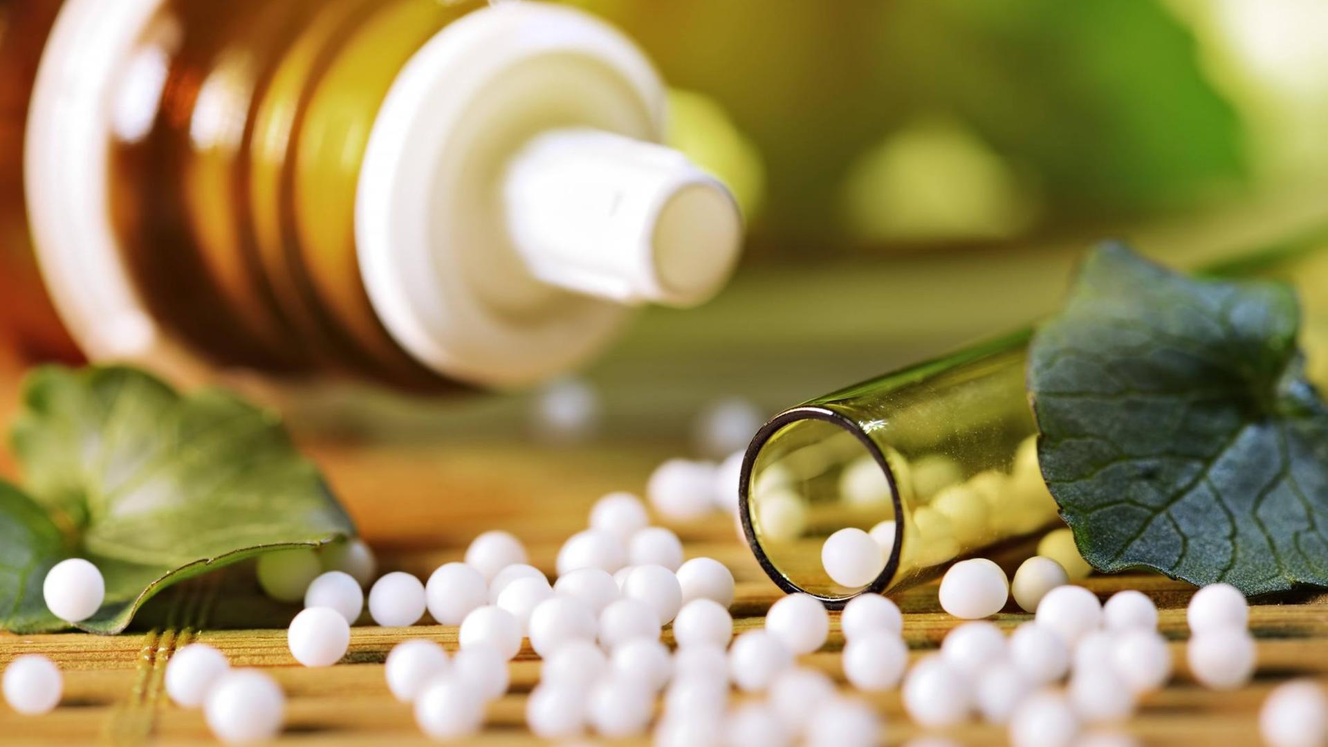 Globuli, homöopathische Kügelchen auf einem Tisch, dahinter eine Fläschchen und Kräuterblätter Globuli, homöopathische Kügelchen auf einem Tisch, dahinter eine Fläschchen und Kräuterblätter