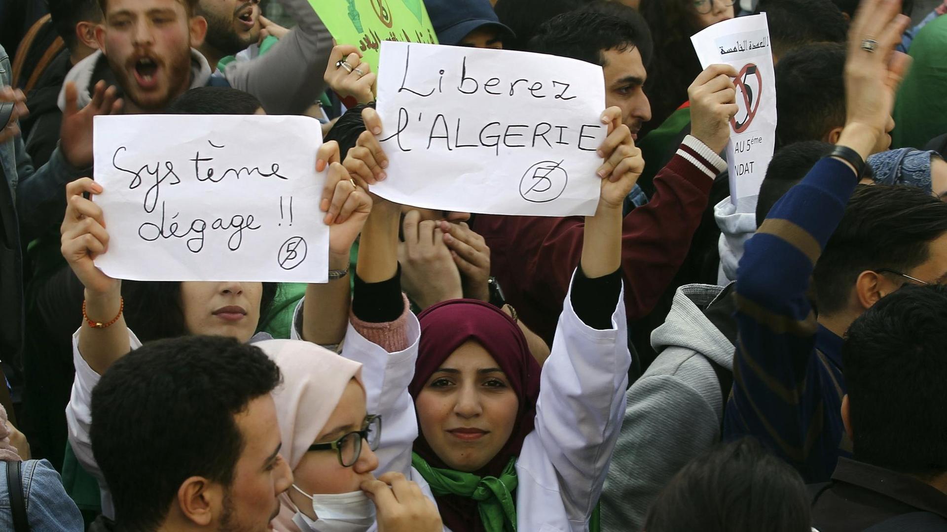 Das Bild zeigt Demonstranten, die Schilder hochhalten. Darauf stehen auf französisch Sprüche zu lesen wie "Befreit Algerien" oder "System - verschwinde".