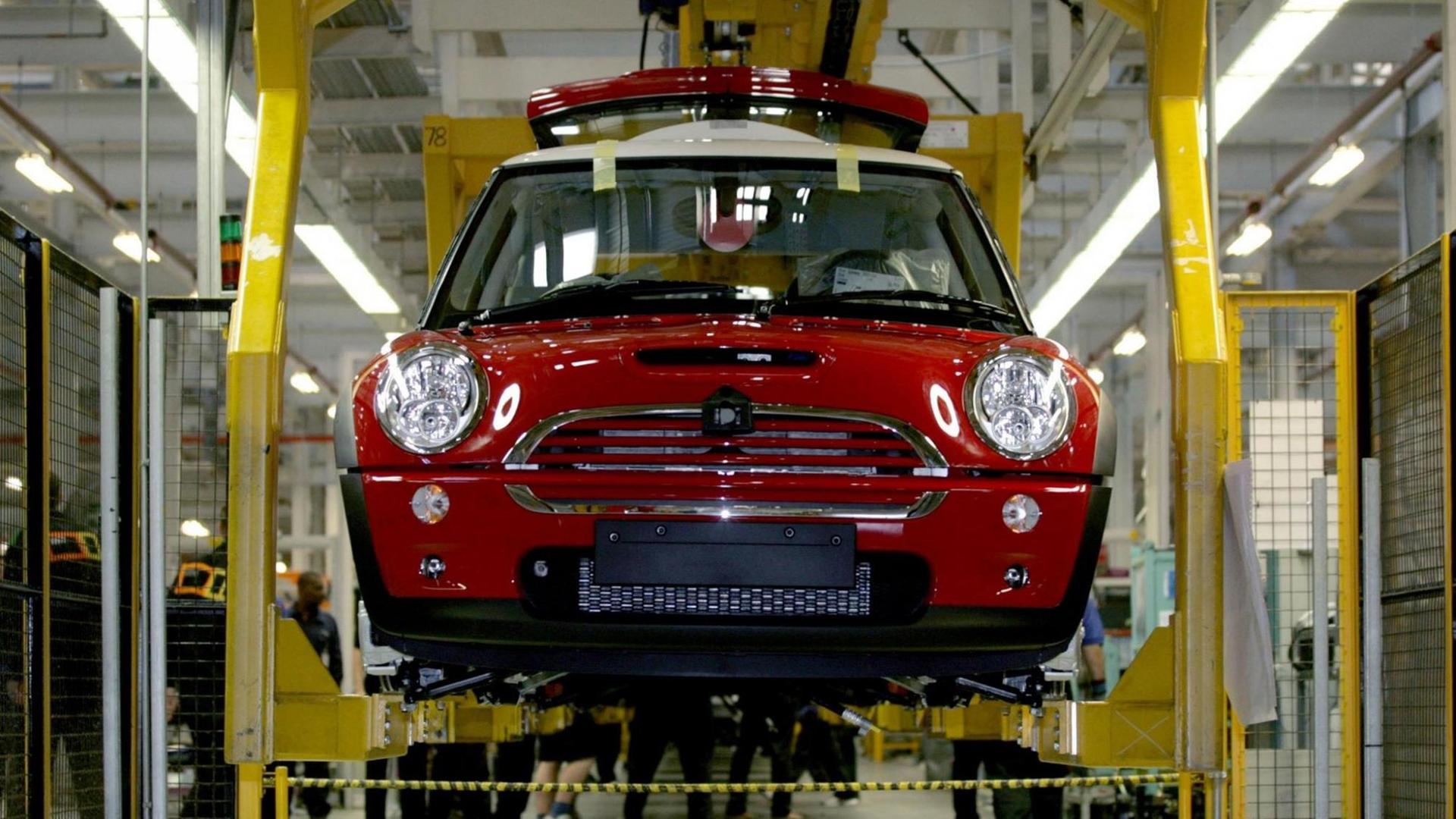 Frontalblick auf einen nahezu fertig montierten roten BMW Mini in einer Produktionsstraße, die Karosserie hängt in einem gelben Gestell, im Hintergrund sind Arbeiter zu sehen. Frontalblick auf einen nahezu fertig montierten roten BMW Mini in einer Produktionsstraße, die Karosserie hängt in einem gelben Gestell, im Hintergrund sind Arbeiter zu sehen.
