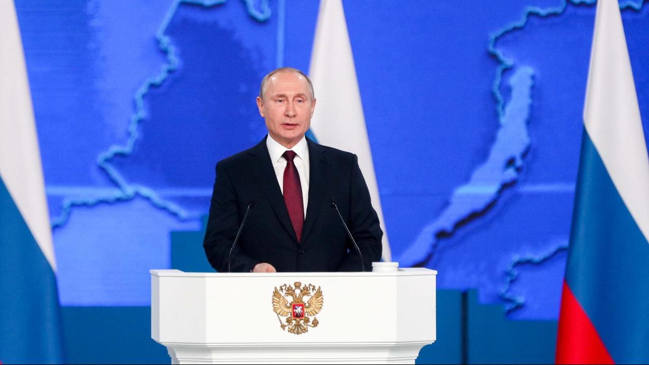 Der russische Präsident Putin steht an einem Rednerpult und spricht. Im Hintergrund sind mehrere russische Flaggen zu sehen. Der russische Präsident Putin steht an einem Rednerpult und spricht. Im Hintergrund sind mehrere russische Flaggen zu sehen.