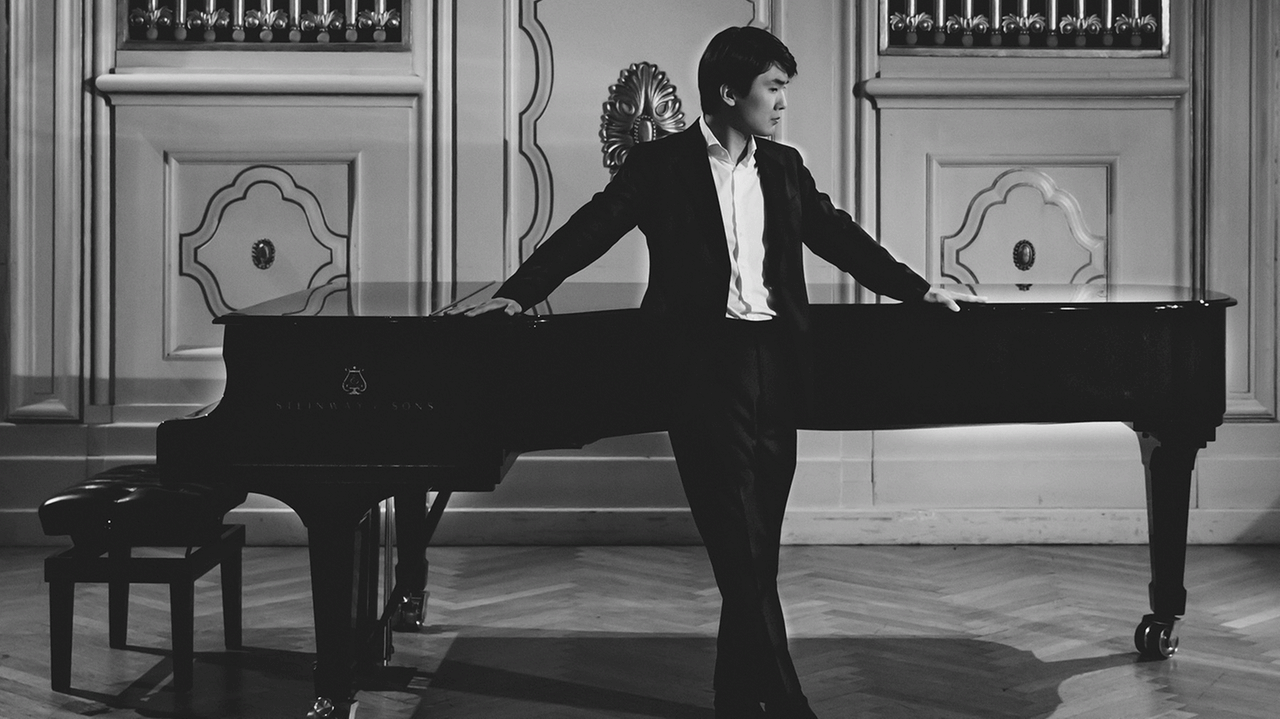Ein junger Pianist Seong-Jin Cho steht vor einem Klavier in einem Konzertsaal, im Hintergrund eine Orgel.