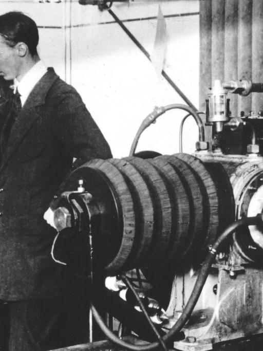 Auf einer historischen Fotografie sind zwei Männer zu sehen, die an technischen Geräten beschäftigt sind.