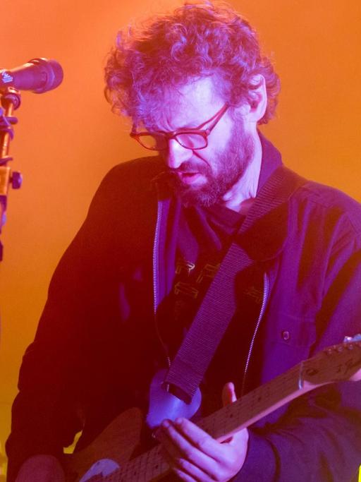 Ein Mann steht auf einer Bühne, schaut auf die Gitarre in seinen Händen.