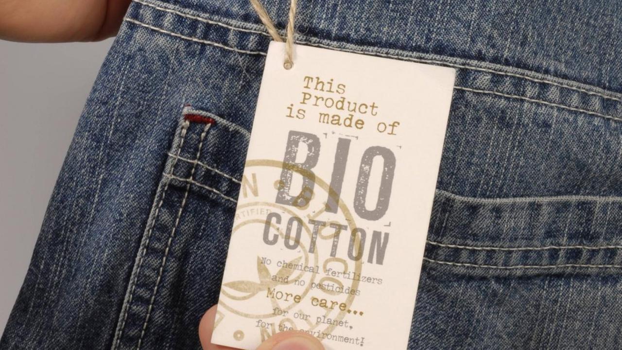 Hände zeigen eine auf ein Bio-Cotton-Label an einer Jeans Hände zeigen eine auf ein Bio-Cotton-Label an einer Jeans