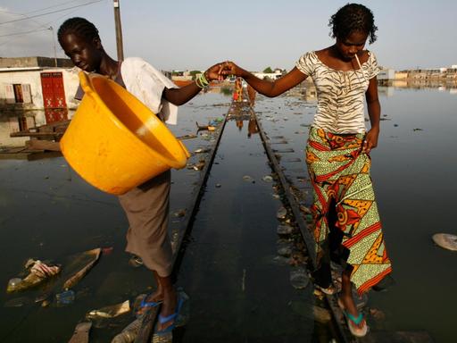 Zwei afrikanische Frauen inmitten einer überschwemmten Wohngegend.