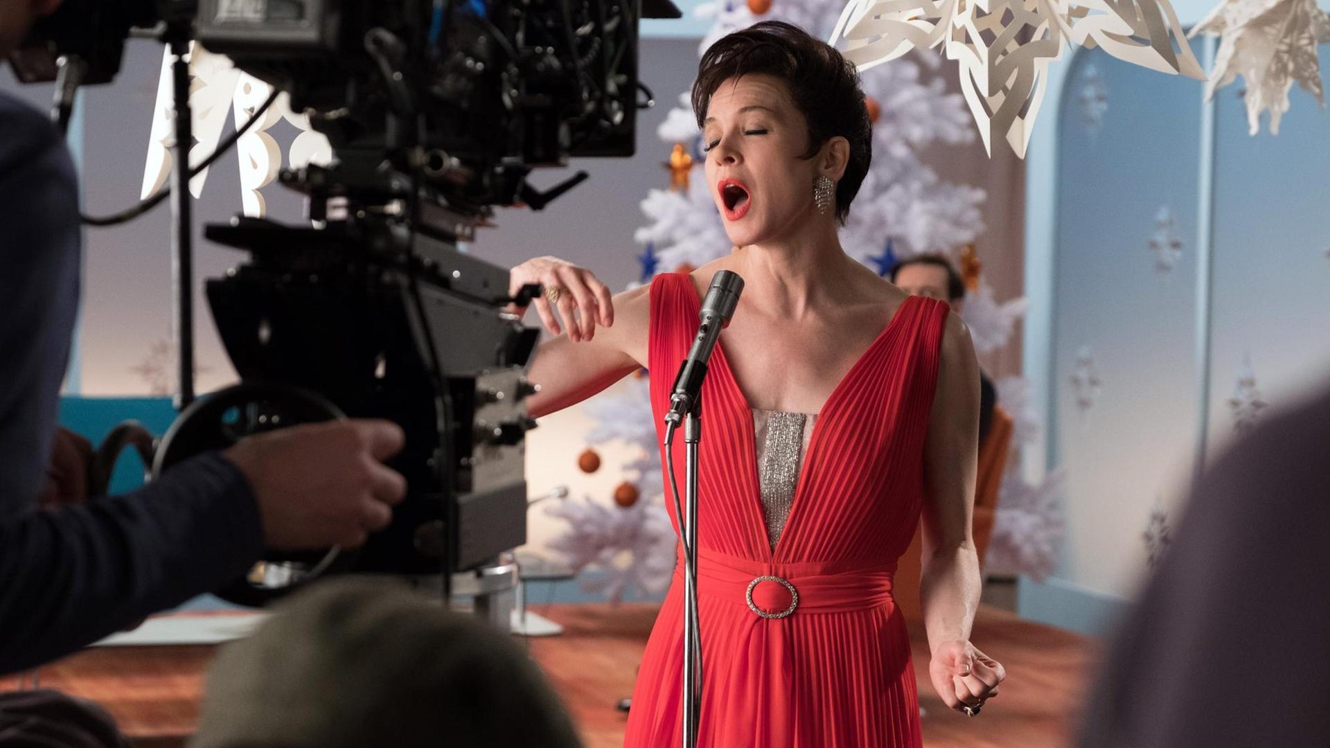 Renee Zellweger steht im roten Kleid vor einer Kamera und singt
