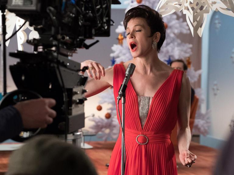 Renee Zellweger steht im roten Kleid vor einer Kamera und singt