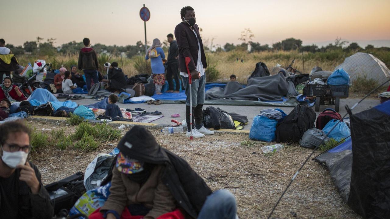 Menschen liegen und stehen am Rande einer Straße in der Nähe des ausgebrannten Flüchtlingslagers Moria aus. Menschen liegen und stehen am Rande einer Straße in der Nähe des ausgebrannten Flüchtlingslagers Moria aus.