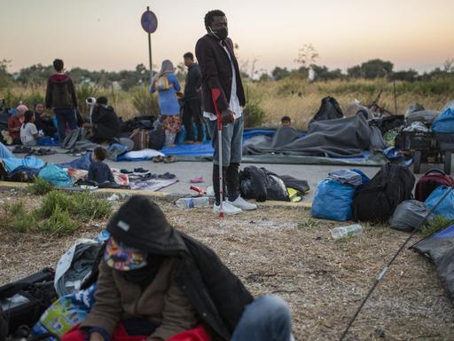 Menschen liegen und stehen am Rande einer Straße in der Nähe des ausgebrannten Flüchtlingslagers Moria aus.