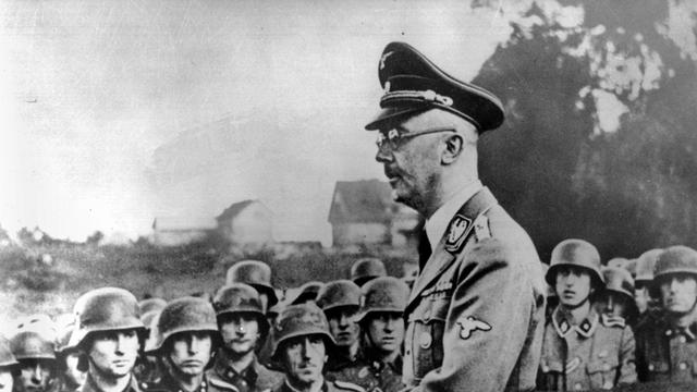 Der NS-Verbrecher Heinrich Himmler, im Hintergrund Soldaten.