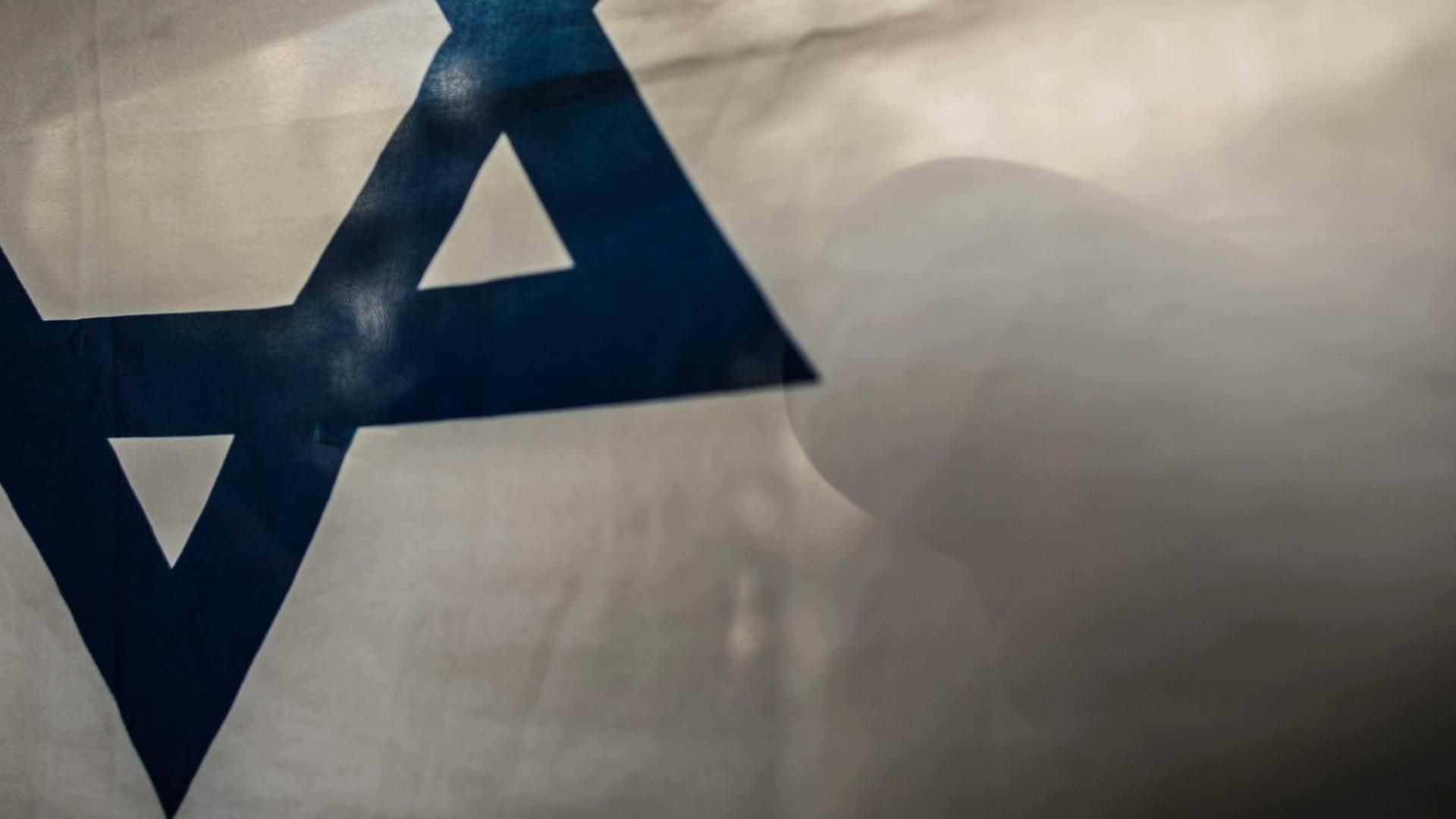 Auf der israelische Flagge spiegelt sich der Schatten einer Person Auf der israelische Flagge spiegelt sich der Schatten einer Person