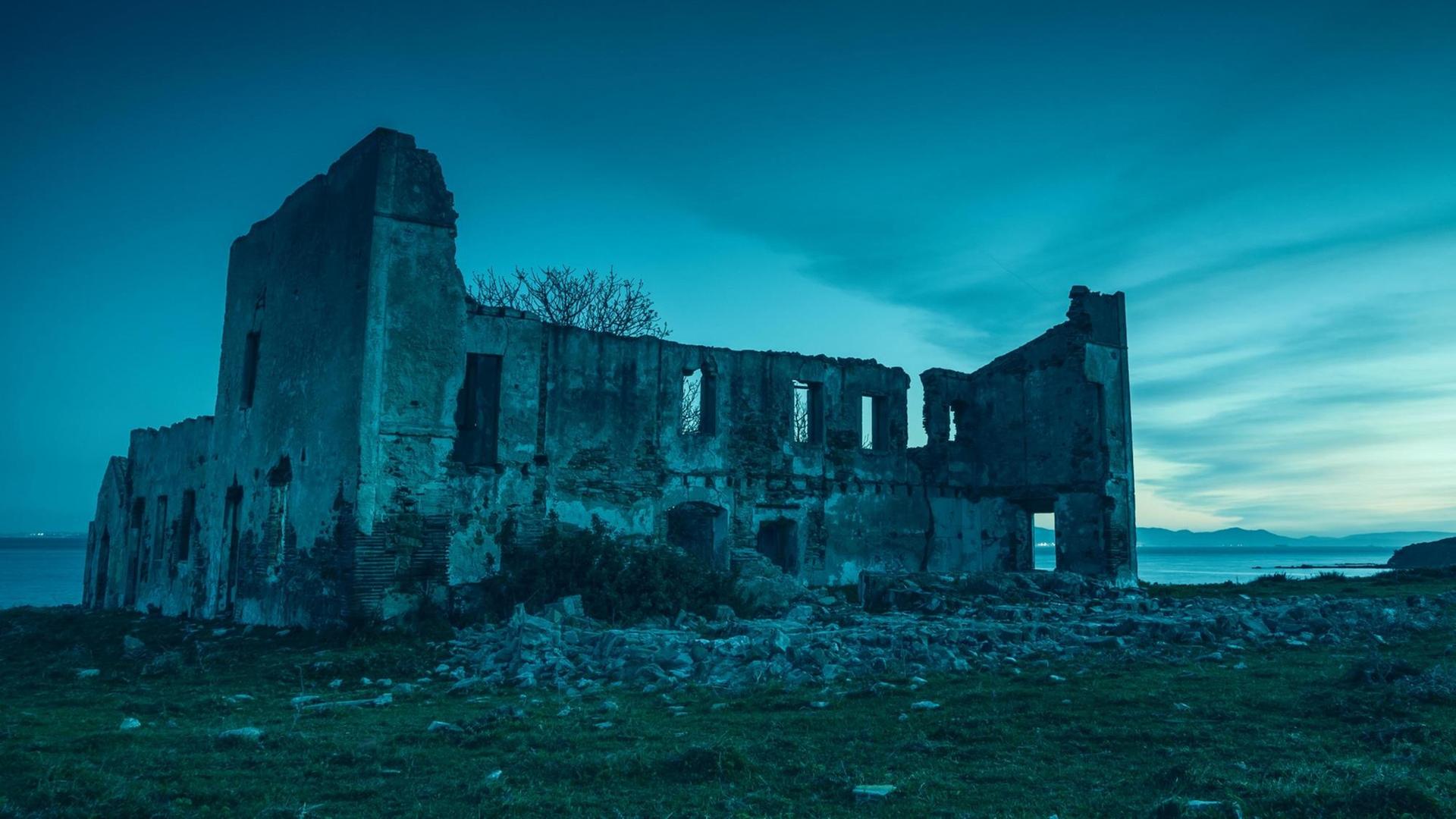 Unheimliche Ruine eines verlassenen Hauses am Meer; ein bläuliches Licht liegt auf alten Mauern Unheimliche Ruine eines verlassenen Hauses am Meer; ein bläuliches Licht liegt auf alten Mauern