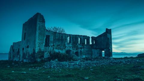 Unheimliche Ruine eines verlassenen Hauses am Meer; ein bläuliches Licht liegt auf alten Mauern