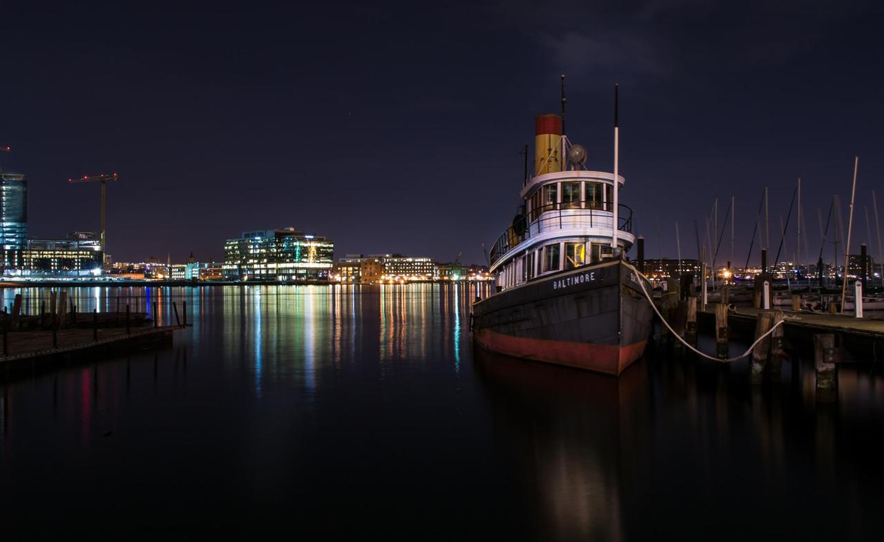 Stimmung bei Nacht mit Blick über das Wasser auf die Stadt Baltimore. Im Vordergrund ein Boot mit der Aufschrift Baltimore.