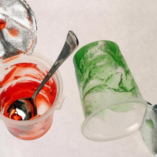 Zwei leere Plastikbecher mit Resten von grüner und roter Götterspeise.