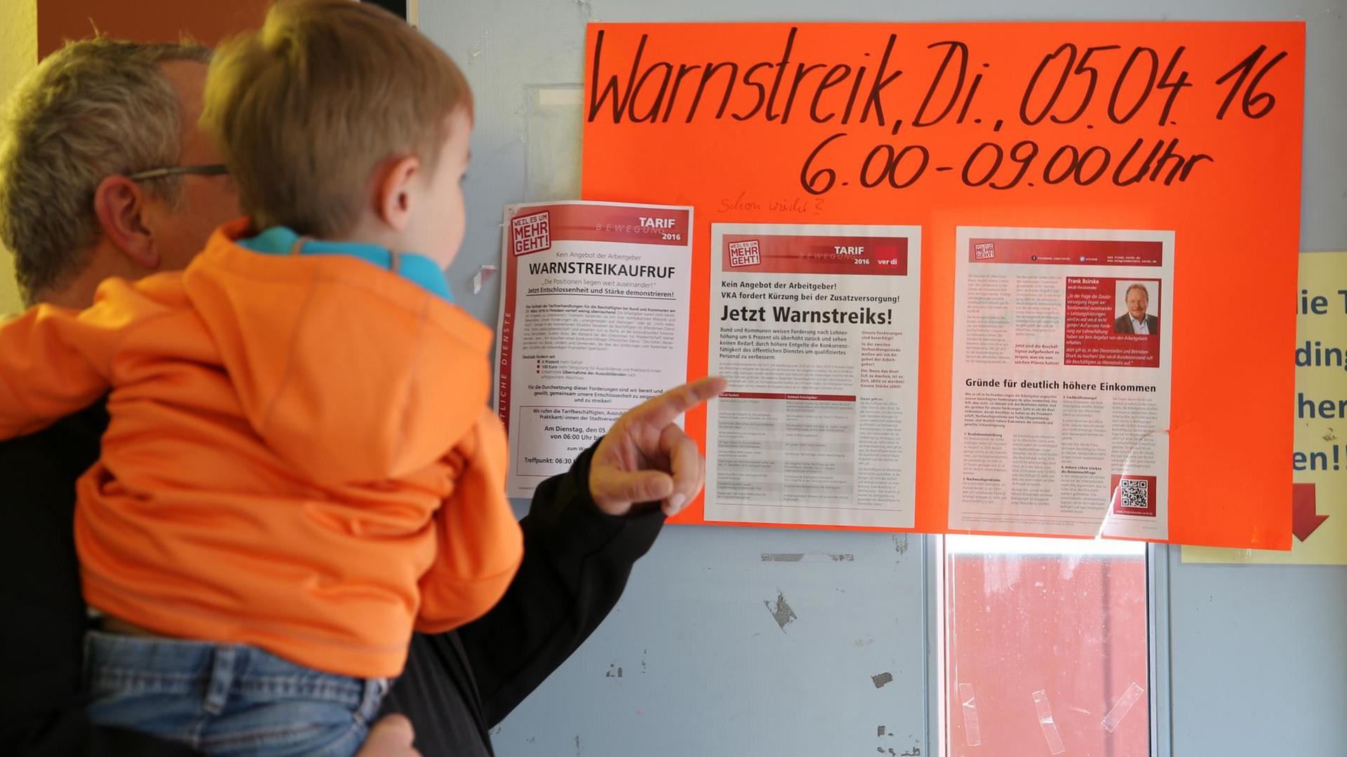 Ein Vater steht mit einem Jungen auf dem Arm am 05.04.2016 vor einem Warnstreikaufruf in einem Kindergarten in Leipzig.