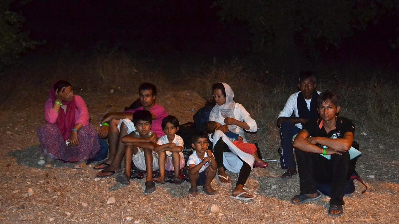 Flüchtlinge sind aus dem Lager Moria geflohen. Dort war an mehreren Stellen feuer ausgebrochen. Erwachsene und Kinder sitzen auf einem Feld.