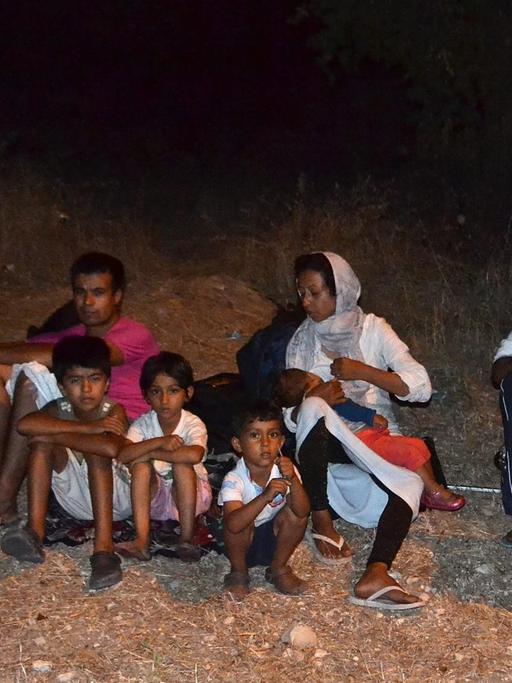 Flüchtlinge sind aus dem Lager Moria geflohen. Dort war an mehreren Stellen feuer ausgebrochen. Erwachsene und Kinder sitzen auf einem Feld.