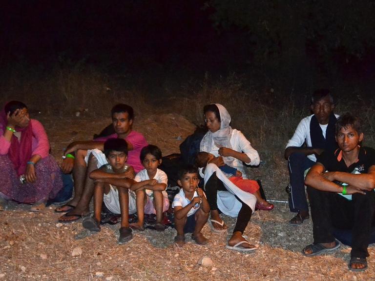 Flüchtlinge sind aus dem Lager Moria geflohen. Dort war an mehreren Stellen feuer ausgebrochen. Erwachsene und Kinder sitzen auf einem Feld.