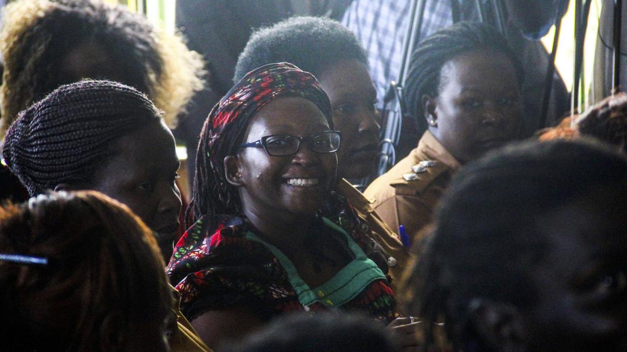 Stella Nyanzi in bunter Kleidung im Gerichtssaal, umgeben von anderen afrikanischen Frauen. Stella Nyanzi in bunter Kleidung im Gerichtssaal, umgeben von anderen afrikanischen Frauen.