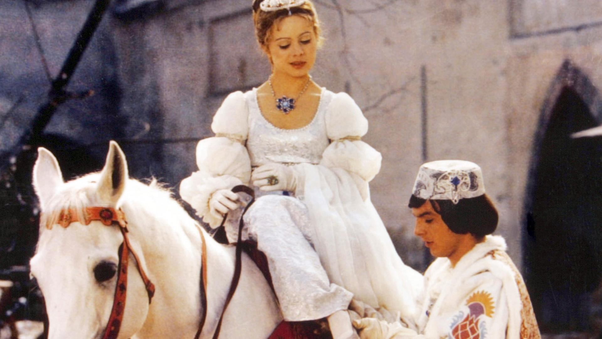 Szene aus dem Film "Drei Haselnüsse für Aschenbrödel": Der Prinz passt Aschenbrödel den verlorenen Schuh an. Sie sitzt dabei auf einem weißen Pferd und blickt zu ihm hinunter. Szene aus dem Film "Drei Haselnüsse für Aschenbrödel": Der Prinz passt Aschenbrödel den verlorenen Schuh an. Sie sitzt dabei auf einem weißen Pferd und blickt zu ihm hinunter.