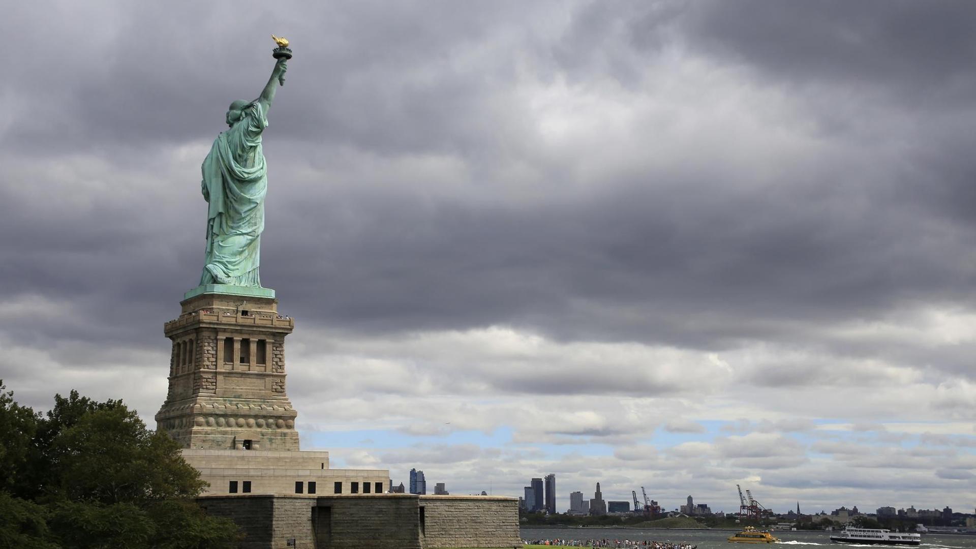 Die Freiheitsstatue auf Liberty Island auf ihrem Sockel, im Hintergrund angedeutet die Skyline von New York Die Freiheitsstatue auf Liberty Island auf ihrem Sockel, im Hintergrund angedeutet die Skyline von New York