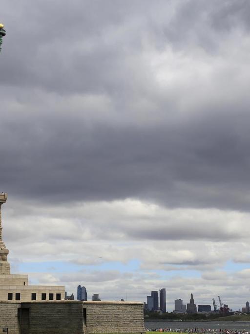 Die Freiheitsstatue auf Liberty Island auf ihrem Sockel, im Hintergrund angedeutet die Skyline von New York