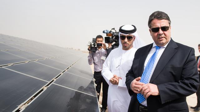 Bundeswirtschaftsminister Sigmar Gabriel, Sonnenbrille tragend, mit Ahmad Belhoul, dem Geschäftsführer des Masdar-Projekts, neben einem Solarfeld stehend.