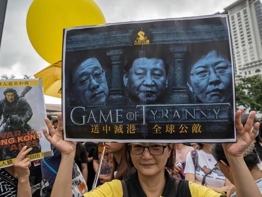 Demonstranten in Hongkong halten ein Schild in die Höhe mit dem die lokale Regierung und er chinesische Staatschef Xi Jinping kritisiert werden.