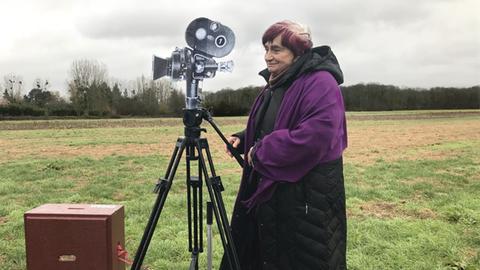 Agnes Varda steht auf einem Kamerawagen der auf Schienen in einer Landschaft steht.