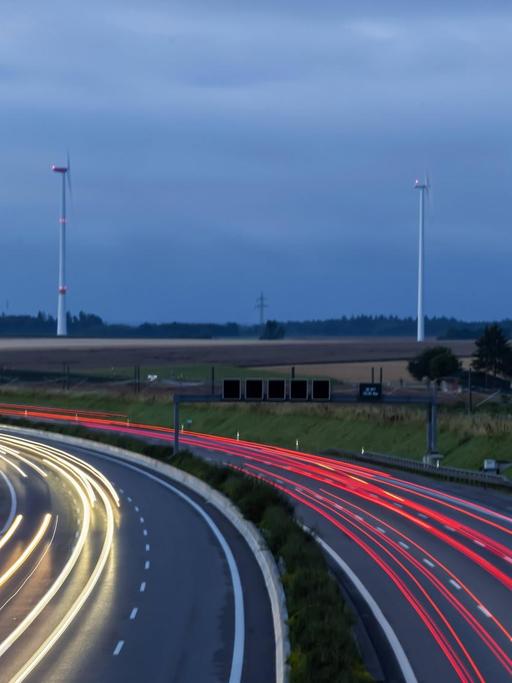 Autobahn A8 am frühen Morgen mit Lichtspuren der Autos. Im Hintergrund ein Windpark.