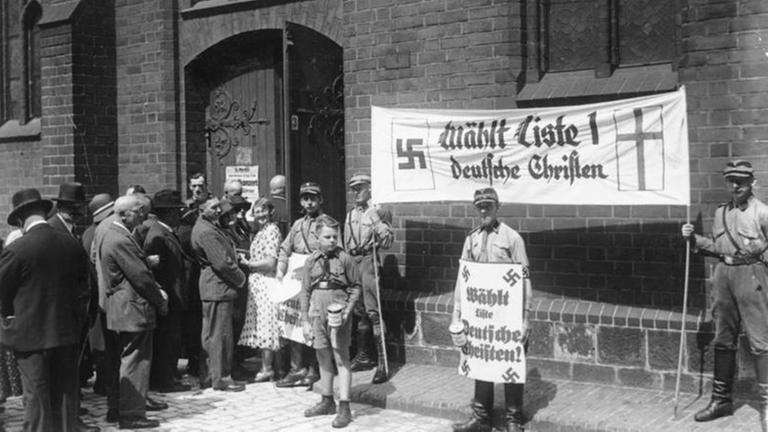Kirchenwahl in Berlin.- SA-Männer vor Marienkirche mit Plakat "Wählt Liste 1 Deutsche Christen". Hitlerjunge mit Spendendose Kirchenwahl in Berlin.- SA-Männer vor Marienkirche mit Plakat "Wählt Liste 1 Deutsche Christen". Hitlerjunge mit Spendendose