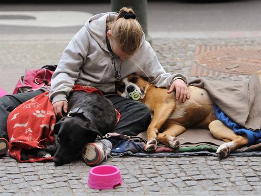 Eine Frau sitzt mit ihren zwei Hunden am Straßenrand.
