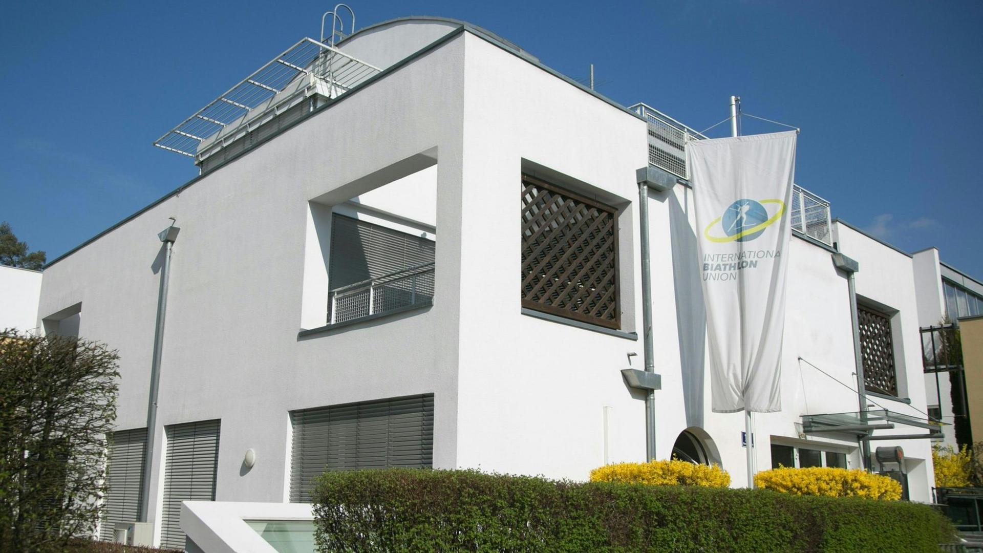 Ds Bild zeigt den Sitz der Internationalen Biathlon Union (IBU) im österreichischen Salzburg. Zu sehen ist eine weiße Fassade hinter einer grünen Hecke.