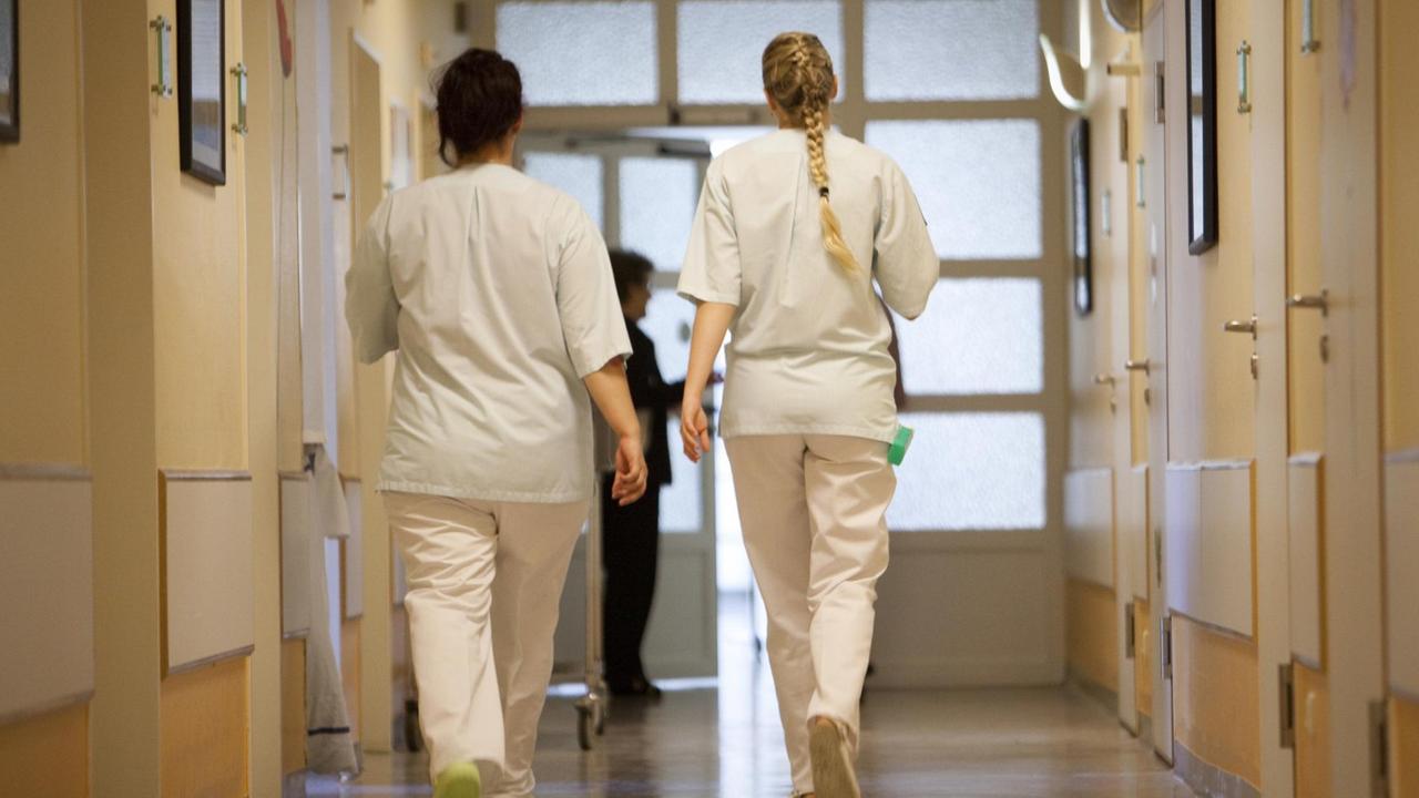 Ein junge Frau im Freiwilligen sozialen Jahr (FSJ, r) und eine Krankenschwester (l) gehen in einem Krankenhaus in Frankfurt am Main gemeinsam einen Korridor entlang. Aufnahme von 2009.