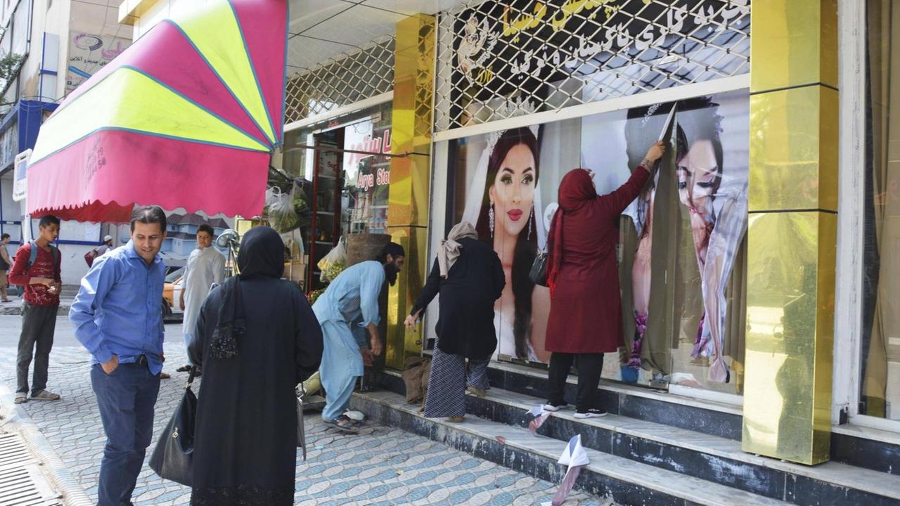 Frauen in Kabul entfernen am 15.08.2021 Plakate an einem Schönheitssalon, die geschminkte und ihre Haare offen tragende Models zeigen. Frauen in Kabul entfernen am 15.08.2021 Plakate an einem Schönheitssalon, die geschminkte und ihre Haare offen tragende Models zeigen.