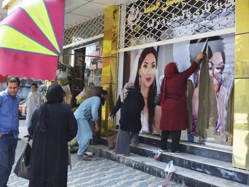 Frauen in Kabul entfernen am 15.08.2021 Plakate an einem Schönheitssalon, die geschminkte und ihre Haare offen tragende Models zeigen.