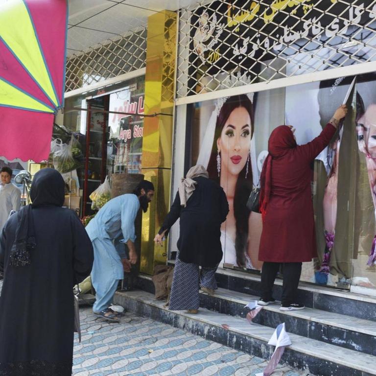 Frauen in Kabul entfernen am 15.08.2021 Plakate an einem Schönheitssalon, die geschminkte und ihre Haare offen tragende Models zeigen.