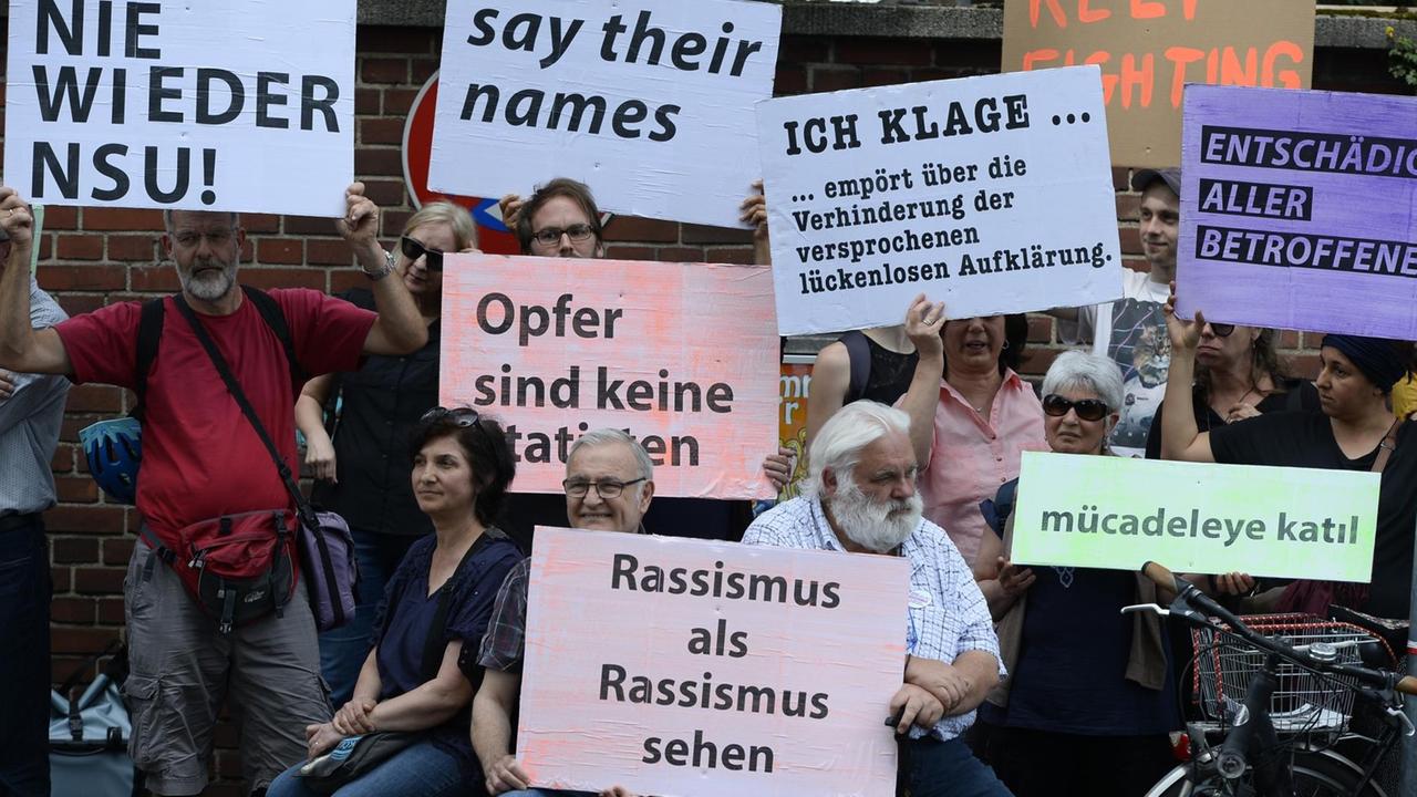 Teilnehmer einer Schweigeminute erinnern mit Plakaten auf der Kölner Keupstrasse am 15. Jahrestag an den NSU-Nagelbombenanschlag