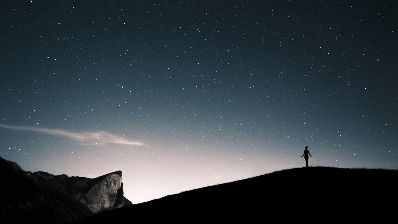 Silhouette einer Frau unter einem Sternenhimmel in den Bergen Silhouette einer Frau unter einem Sternenhimmel in den Bergen